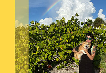 Drea holding her dog in front of a rainbow